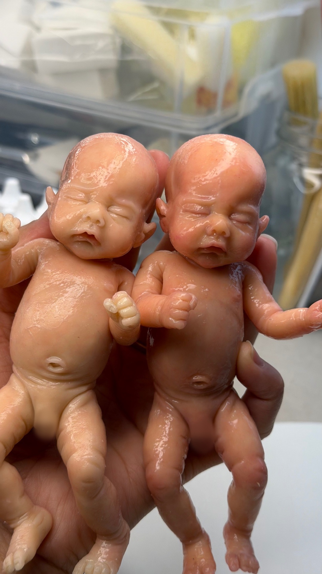 Two miniature silicone babies held in the artist's hand